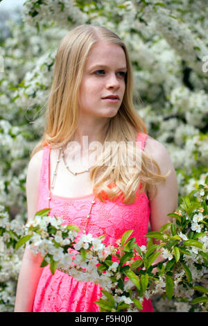 Blonde Frau in einem rosa Kleid posiert innerhalb der Blumen während des Sommers. Stockfoto