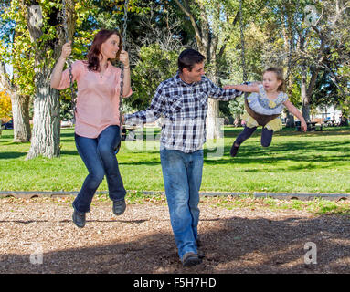 Vater, Mutter und niedliche kleine Tochter spielen auf Park schwingt Stockfoto