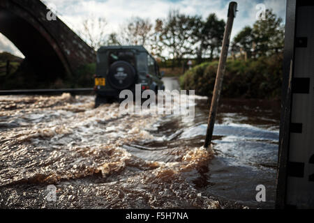 Land Rover fährt durch eine Furt, wie ein Stream eine Straße überquert. Stockfoto