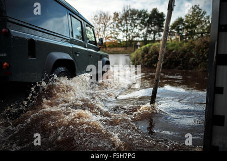 Land Rover fährt durch eine Furt, wie ein Stream eine Straße überquert. Stockfoto