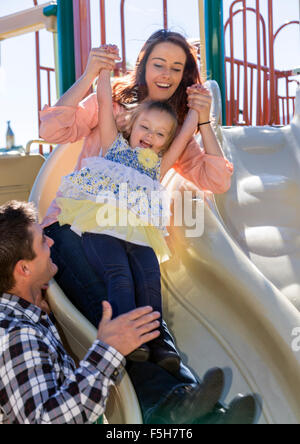 Schöne Mutter und niedliche junge Tochter Mädchen spielen im Freien auf die sliding Board, Stadtpark Stockfoto