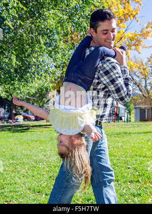 Vater, spielerisch tragen junge Tochter auf dem Kopf stehend im park Stockfoto