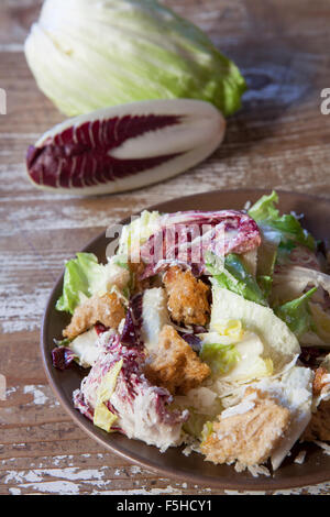 Chicorée-Caesar-Salat mit Croutons auf Teller mit Chicorée im Hintergrund. Stockfoto