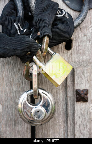 Nahaufnahme von Doppel mit einem Vorhängeschloss Kette zu zwei offene Tür verbunden griff Ringe, in alte Holztür. Stockfoto