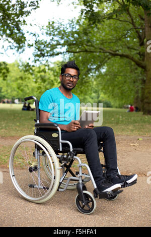 junger Mann in einem Rollstuhl mit einem Tabletcomputer Stockfoto