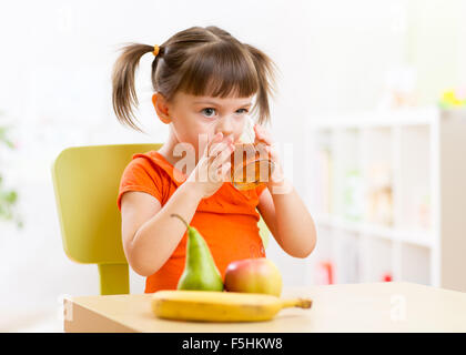 Lächelndes Kind Mädchen auf dem Tisch mit Früchten und trinken Saft im Kindergarten Stockfoto