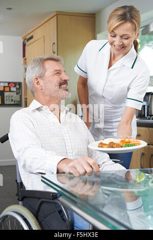Pflegeperson servieren Mahlzeit Mann im Rollstuhl zu Hause Stockfoto