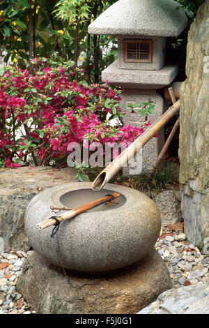 Japanisches Wasserspiel aus Bambus-Rohr und kreisförmige Stein Topf auf der Terrasse mit einer Steinlaterne Stockfoto