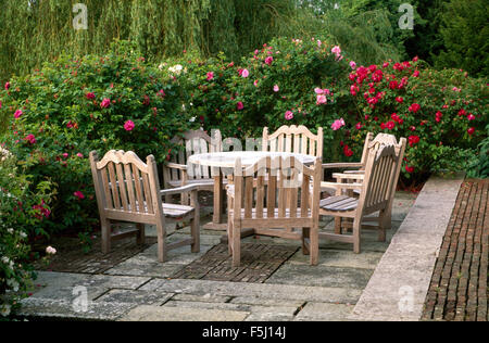 Schweren Holztisch und Stühle auf einem gepflasterten Land Terrasse umgeben von rosa Rosen Stockfoto