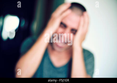 ein unscharfes Bild von einem jungen kaukasischen Mann mit seinen Händen in den Kopf und schreiend im Innenbereich Stockfoto