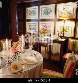 Tisch für das Abendessen mit Kerzen in graviertes Glas Laternen im Esszimmer mit einer Gruppe von floralen Prints an der Wand der achtziger Jahre Stockfoto