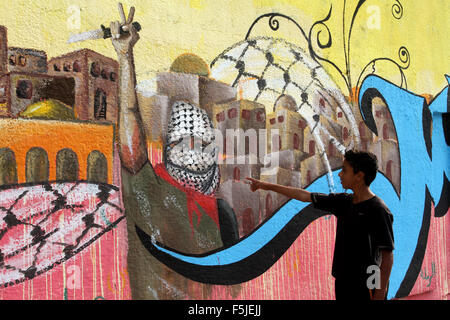 Rafah, Gaza-Streifen, Palästinensische Gebiete. 5. November 2015. Ein palästinensischer Jugendlicher steht vor einem Graffiti Darstellung einen maskierten Palästinenser mit einem Messer, zur Unterstützung der dritten palästinensischen Aufstand in Rafah im südlichen Gazastreifen 5. November 2015. Die aktuelle Welle von Gewalt brach Mitte September, angeheizt durch Gerüchte, die Israel versuchte, die jüdische Präsenz in Jerusalem zu erhöhen dann schnell verbreitet über Israel, das Westjordanland und den Gaza-Streifen Kredit: Abed Rahim Khatib/APA Bilder/ZUMA Draht/Alamy Live News Stockfoto