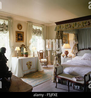 Himmelbett mit weißer Bettwäsche und floral Gardinen in einer opulenten achtziger Jahre Schlafzimmer mit Lampen und ein weißes Tuch auf den Tisch Stockfoto