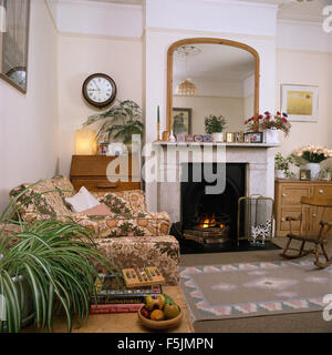 Spiegel über dem Marmorkamin mit brennenden Feuer im Wohnzimmer der neunziger Jahre Stockfoto