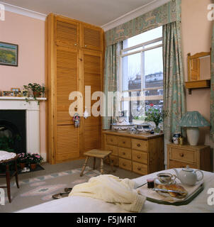 Louvre Türen am Schrank neben offenen Schiebefenster in einer neunziger Jahre Schlafzimmer Stadthaus mit einem Frühstückstablett auf Bett Stockfoto