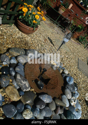 Nahaufnahme von einem kleinen Brunnen in einem Kies-Pool in einem Innenhof mit einem Topf orange Ringelblumen Stockfoto
