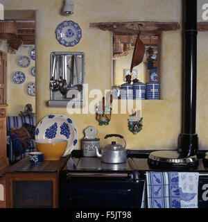 Blau + weiß Keramik Gläser auf eine kleine innere Fensterbank über Aga-Ofen mit einem Aluminium Wasserkocher in einer Ninetiescottage Küche Stockfoto