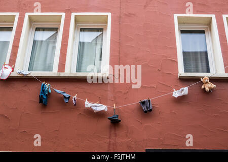 Kinderkleidung und ein Teddybär auf einer Wäscheleine vor den Fenstern eines Hauses, Saarburg, Rheinland-Pfalz, Deutschland Stockfoto