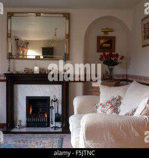 Vergoldeter Spiegel über Kamin mit angezündeten Feuer in einer neunziger Jahre Wohnzimmer mit weißen Sofa und einer kleinen Nische Stockfoto