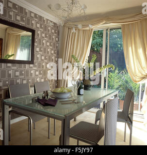 Metall-Stühle und Tisch im Speisesaal mit grauen abstrakte Mustertapeten und cremefarbene Vorhänge auf Glas Terrassentüren aus Glas gekrönt Stockfoto