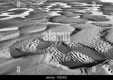 Sand plätschert und Becken am Strand mit Meerwasser bei Ebbe gefüllt. Schwarz / weiß Stockfoto