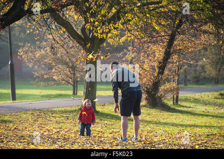 Ein Mann wirft Laub in der Luft für sein Kind in einem Londoner park Stockfoto