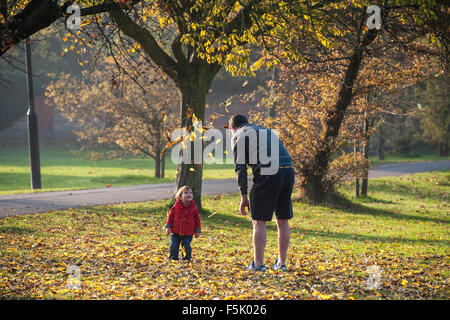 Ein Mann wirft Laub in der Luft für sein Kind in einem Londoner park Stockfoto