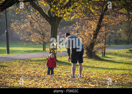 Ein Mann wirft Laub in der Luft für sein Kind in einem Londoner park Stockfoto