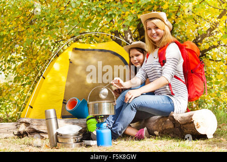 Mädchen kochen Suppe in metallischen Topf sitzt neben Zelt Stockfoto