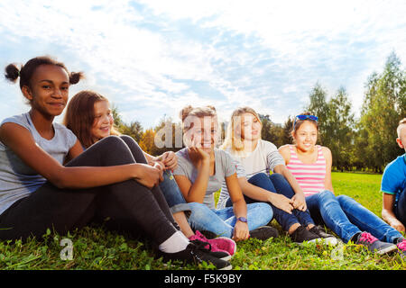 Lächelnde internationale Freunde sitzen auf Rasen Stockfoto