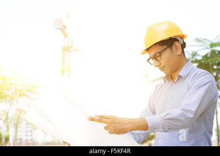 Porträt des asiatischen indischen männlichen Auftragnehmer Ingenieur mit Schutzhelm Lesung Blaupause auf Baustelle. Stockfoto