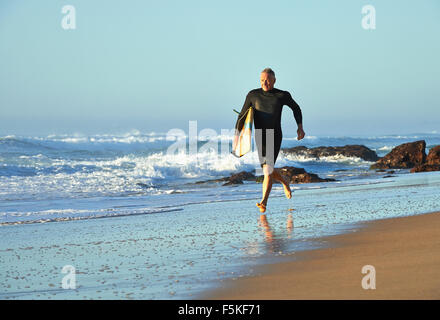 Reifen Alter Mann Joggen am Strand mit einem Surfbrett Stockfoto