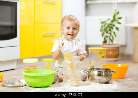 Verspielte Kind Kleinkind mit Gesicht verschmutzt Mehl. Kleiner Junge umgeben, Geschirr und Lebensmittel Stockfoto