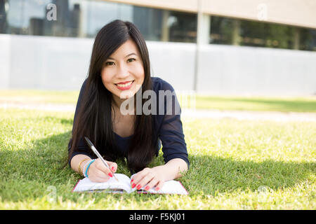 junge japanische Studentin liegen auf dem Rasen mit einem Lehrbuch Stockfoto