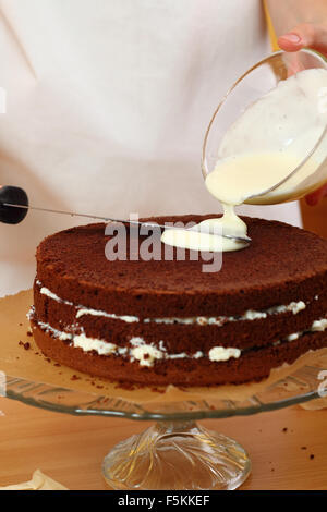 Zuckerguss auf Kuchen gießen. Herstellung von Schokolade Schicht Kuchen. Serie. Stockfoto