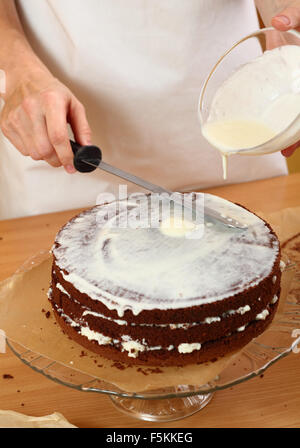 Zuckerguss auf Kuchen gießen. Herstellung von Schokolade Schicht Kuchen. Serie. Stockfoto