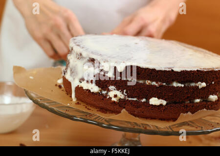 Zuckerguss auf Kuchen gießen. Herstellung von Schokolade Schicht Kuchen. Serie. Stockfoto