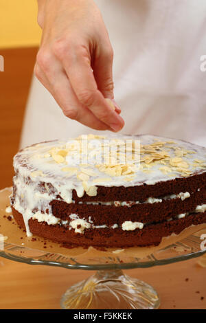 Verbreitung in Scheiben geschnittenen Mandeln und kandierten Orangenschalen. Herstellung von Schokolade Schicht Kuchen. Serie. Stockfoto