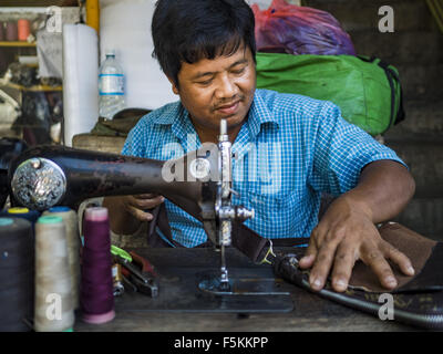 Yangon, Yangon Division, Myanmar. 6. November 2015. Ein Mann repariert Gepäck auf seinem Straßenstand mit einem Pedal angetrieben Nähmaschine. Einige Ökonomen halte Myanmars Schattenwirtschaft größer als die formale Wirtschaft. Viele Menschen sind selbständige in Bargeld nur Unternehmen wie Suppen, gelegentliche Arbeit und Arbeit, Betel zu verkaufen, oder Arbeiten aus tragbaren Straßenständen, Dinge zu tun wie Gepäck Reparatur. Trotz der Reformen in Myanmar und die Expansion der Wirtschaft leben die meisten Menschen in der informellen Wirtschaft. Während einer Pressekonferenz in dieser Woche sagte birmanischen Oppositionsführerin Aung San Suu Kyi, Stockfoto