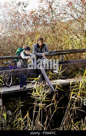 Mutter und Sohn mit Fahrrädern stehen auf hölzernen Steg nach unten am Fluss Stockfoto