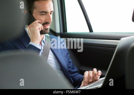 Jungunternehmer im Chat auf Smartphone im Rücksitz des Wagens Stockfoto