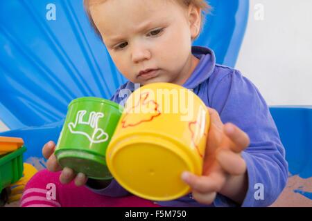 Neugierigen weiblichen Kleinkind mit Tassen im Garten spielen Stockfoto