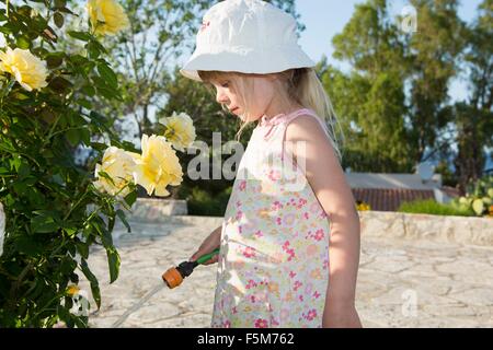 Mädchen tragen Sonnenhut Bewässerung Rosen Stockfoto