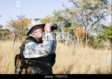 Senior woman Blick durch ein Fernglas auf Safari, Kafue Nationalpark, Sambia Stockfoto