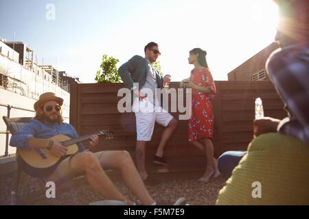 Erwachsenen Freunden chatten und spielen Gitarre auf Party auf dem Dach Stockfoto