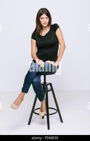 Junge Frau sitzt auf Schemel Blick auf Kamera schmollend Stockfoto
