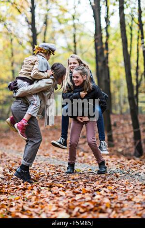 Mutter und Töchter spielen Huckepack Reiten im herbstlichen Wald Stockfoto
