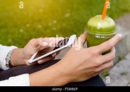 Nahaufnahme von junge Frau sitzt mit Smoothie Drink mit smartphone Stockfoto