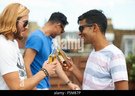 Zwei männliche Freunde machen einen Toast mit Flaschenbier auf Party auf dem Dach Stockfoto