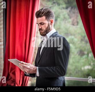 Mitte erwachsener Mann Anzug steht vor Fenster mit digital-Tablette Stockfoto